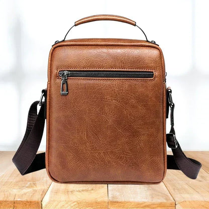 Back of the tan shoulder bag, showing a single zipped pocket, top carry handle and strap attachments. 6