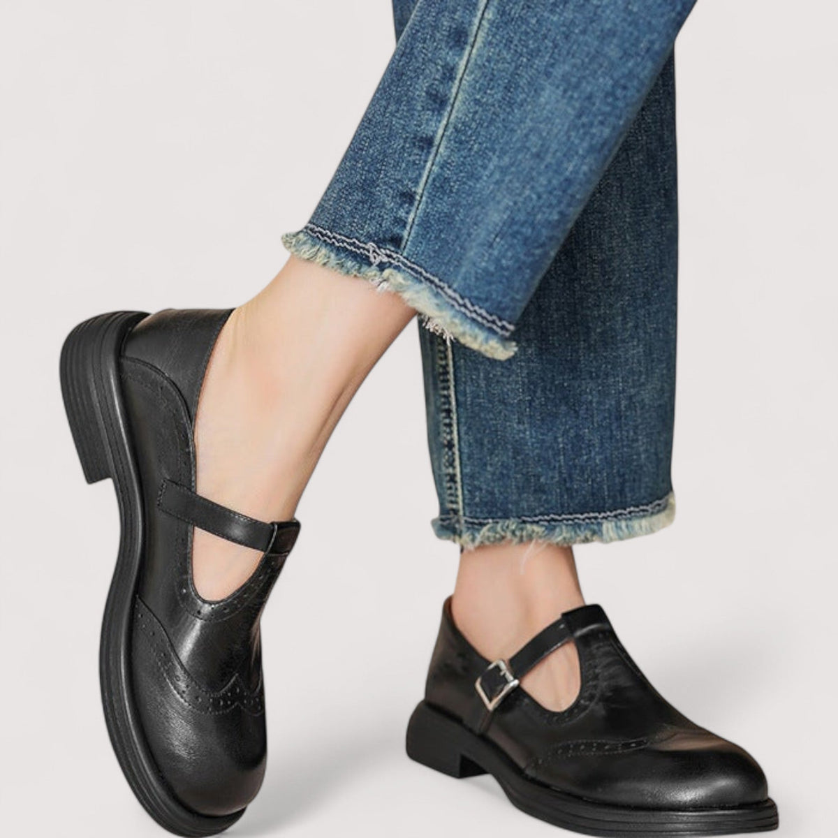 Black brogue Mary Janes with buckled straps worn by a model in cropped, frayed-hem blue jeans. 4