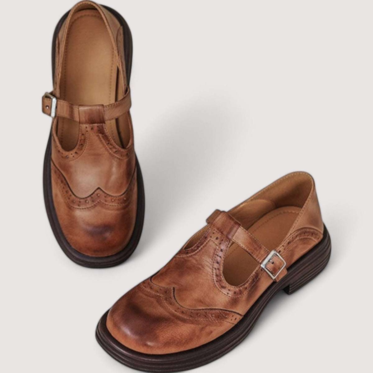 Pair of tan leather brogue Mary Janes seen from above, one showing the buckle strap, the other its tan insole. 2