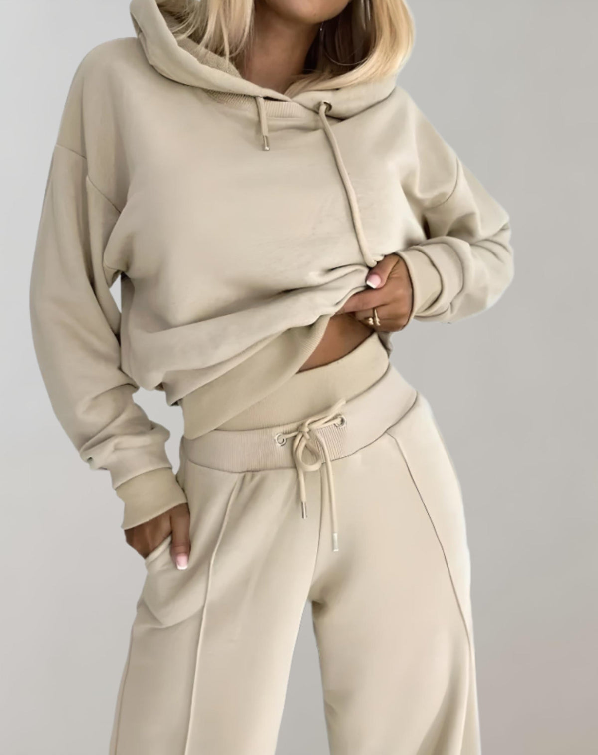 Close-up of the beige set from the chest down, showing the drawstring hood, ribbed waistband with eyelets and trouser seam. 6
