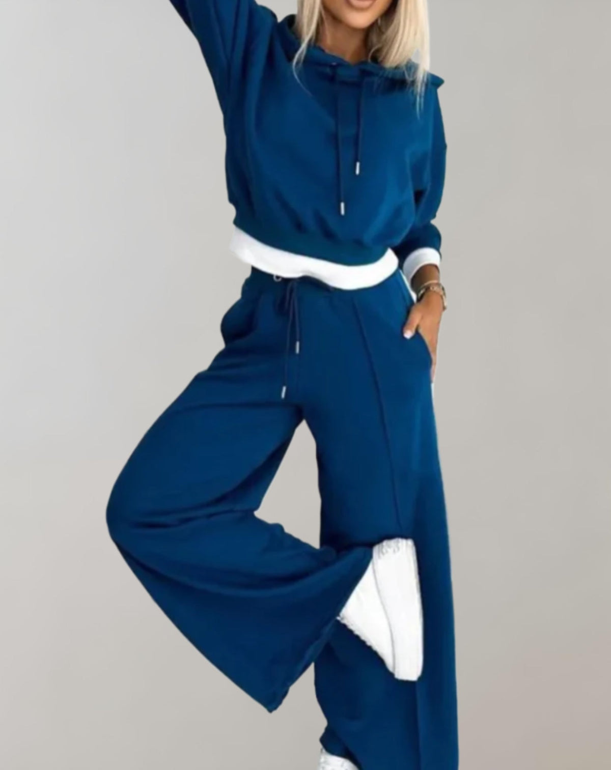Model in the deep blue set with white trim, one arm raised and one leg lifted to show the wide trouser leg. 4