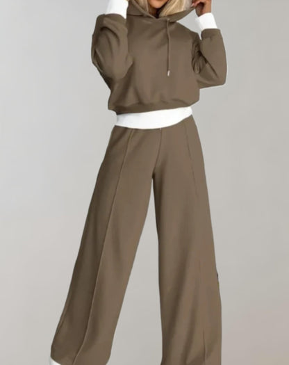 Model wearing the taupe brown set with white cuffs and waistband, holding the hood with both hands. 5