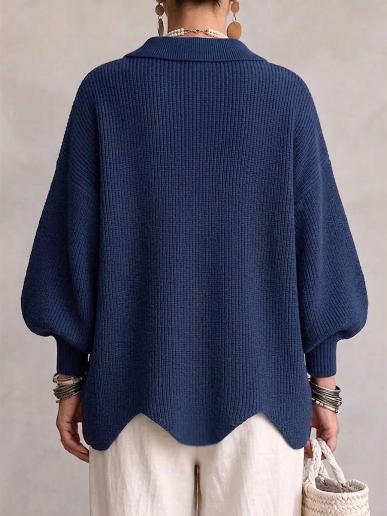 Back view of the navy ribbed cardigan on a model, showing the collar, balloon sleeves and wavy scalloped hem. 2