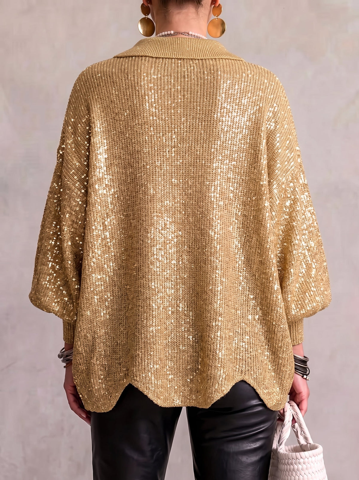 Back view of the gold sequinned cardigan on a model, with shimmering sequins across the knit and a scalloped hem. 6