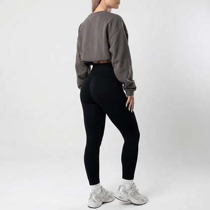 Back view of plain black high-waisted leggings styled with an oversized grey sweatshirt and white socks with silver trainers. 25