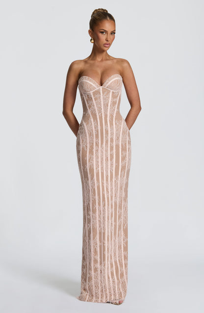 Front view of the blush pink lace version worn with gold earrings, hands behind her back, showing the boned bodice and column skirt. 13