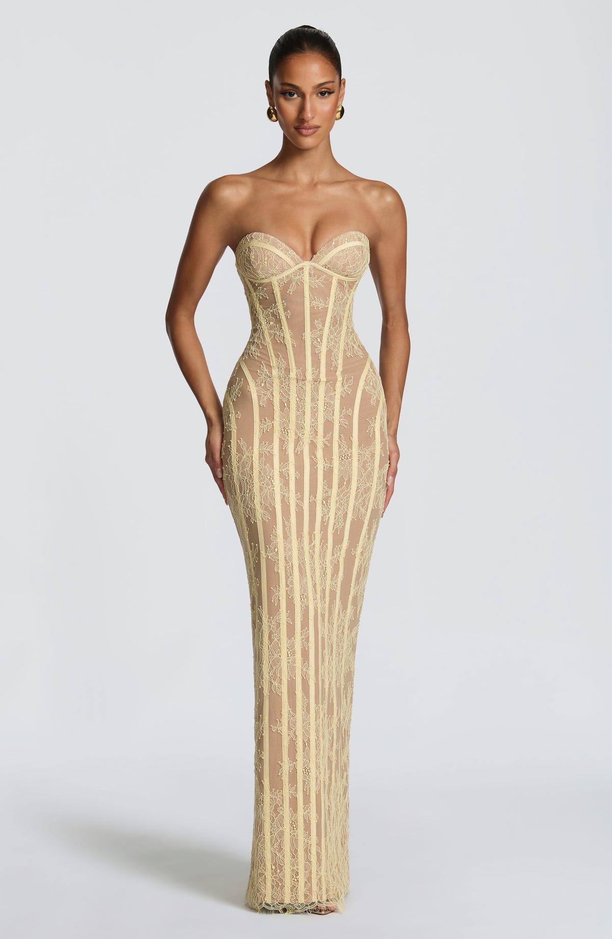 Front view of the pale yellow lace version, with a model in gold earrings, showing the bustier top, vertical boning and fitted maxi skirt. 17