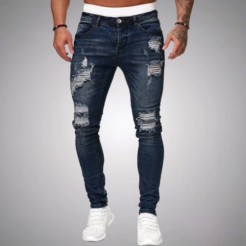 Front view of slim-fit ripped jeans in dark navy blue, worn by a model with white trainers, showing distressed knees and thighs. 4
