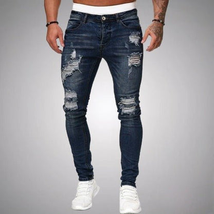 Front view of slim-fit ripped jeans in dark navy blue, worn by a model with white trainers, showing distressed knees and thighs. 4