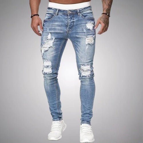 Front view of slim-fit ripped jeans in light blue, worn by a model with white trainers, showing heavy knee and thigh tears. 2