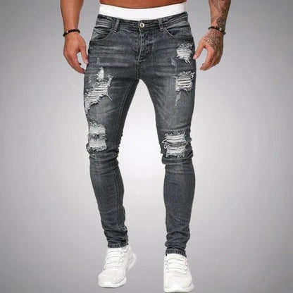 Front view of slim-fit ripped jeans in faded charcoal grey, worn by a model with white trainers, showing frayed rips on the legs. 5