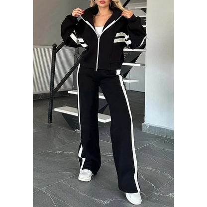 Model in the black set with white stripes, hands on the zipped jacket collar, full-length front view. 3
