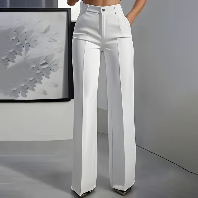 Front view of white high-waisted straight-leg trousers with pressed crease and button waist, worn by a model in a grey room. 3