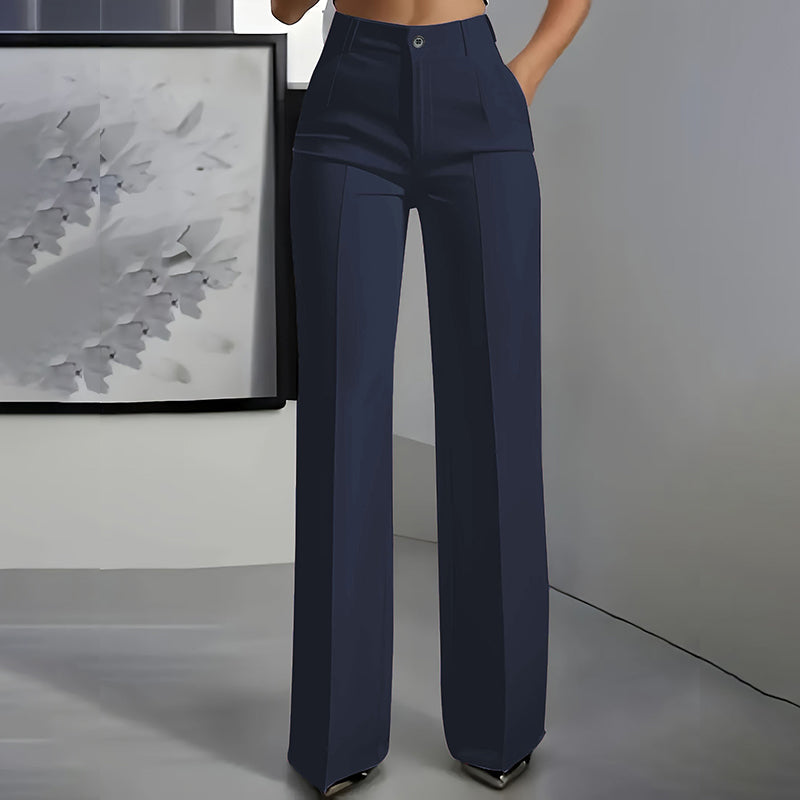 Front view of navy high-waisted straight-leg trousers with centre crease, worn by a model in a grey room with framed artwork. 2