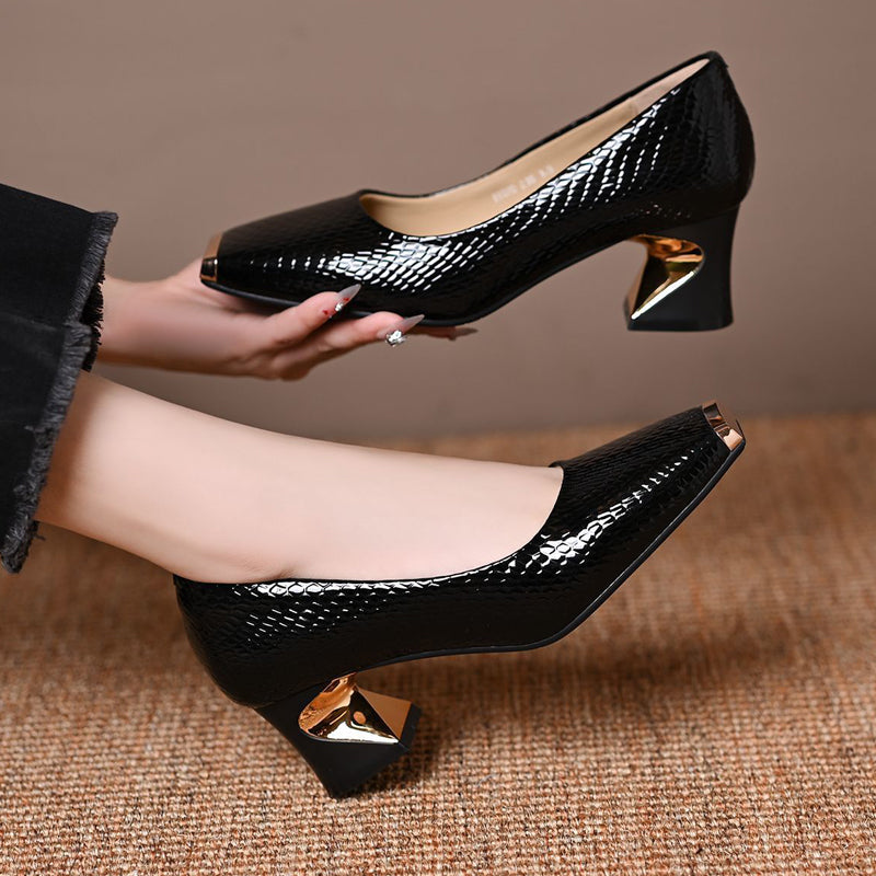 One black snake-effect pump held in a hand above the other worn on a foot, showing the cream lining and angular heel. 5