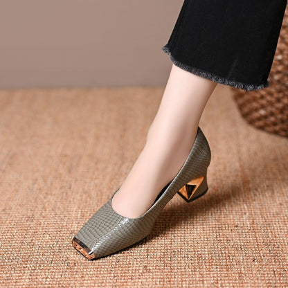 Single grey-green snake-effect pump with a gold metal toe cap and angular gold-detail block heel, worn with frayed black trousers. 3