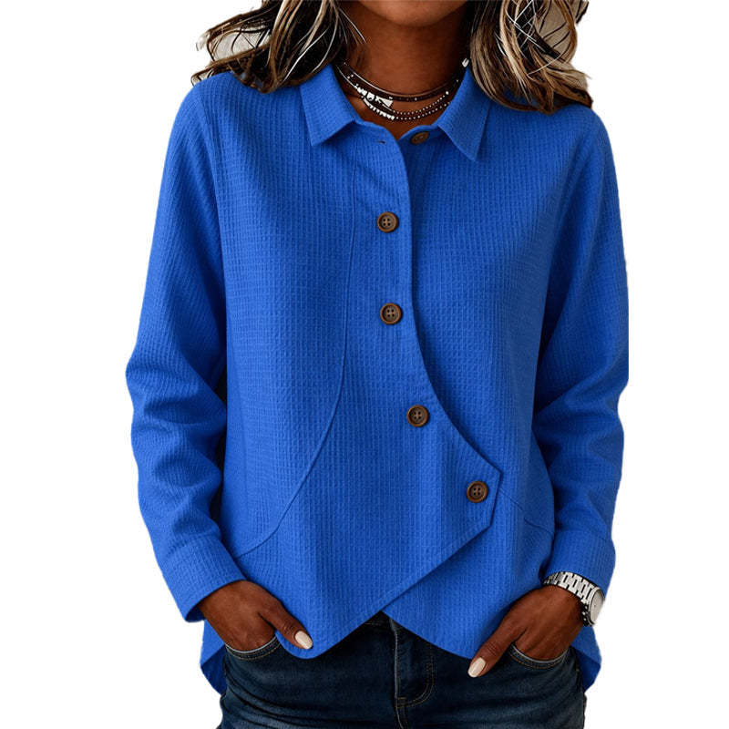 Model wearing the waffle-knit top in bright blue, hands in jeans pockets, showing the collar, brown buttons and curved asymmetric hem. 1