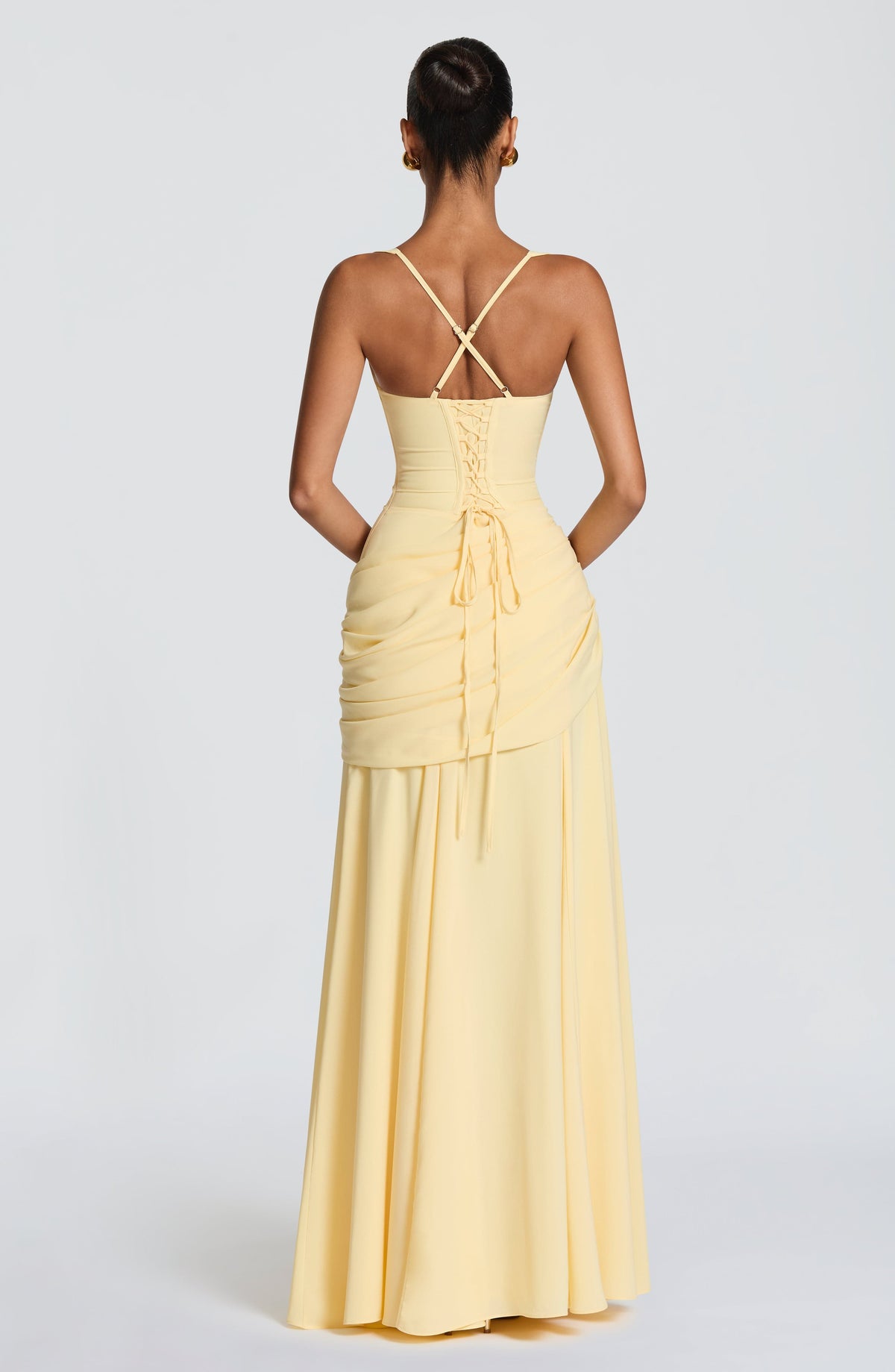 Back view of the pale yellow dress showing the lace-up corset back, crossed thin straps and draped hip panel. 2