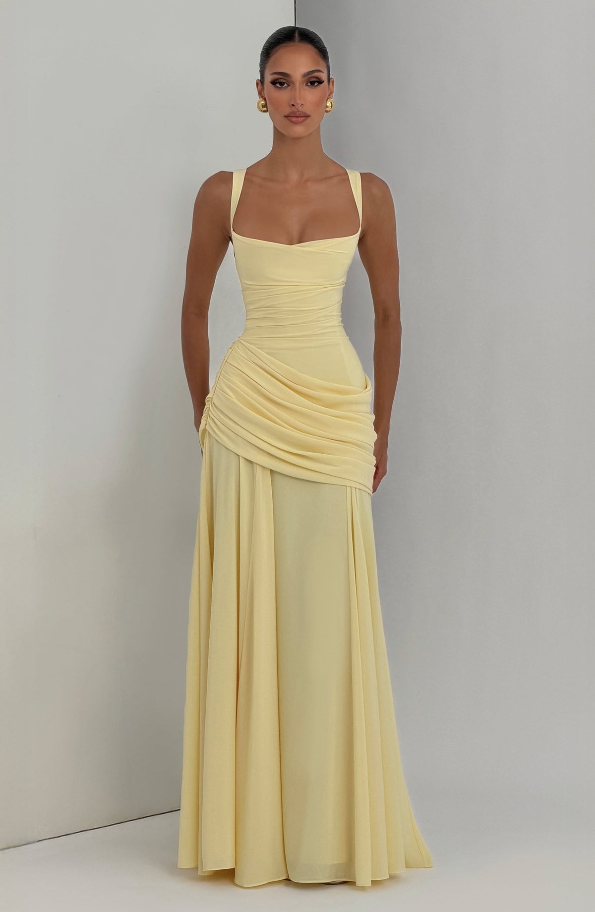 Pale yellow maxi dress worn by a model standing in a studio corner, front view showing the draped waist and flared chiffon skirt. 6