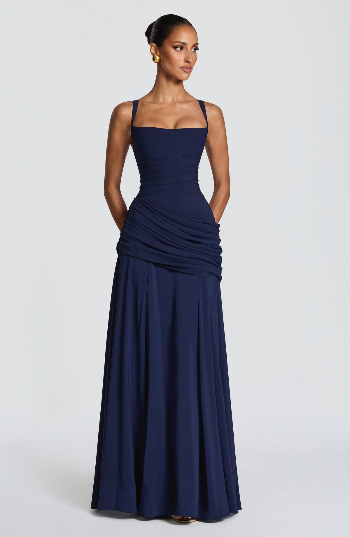 Navy dress on a model with her hands in the pockets, front view showing the draped hip panel and full skirt. 10