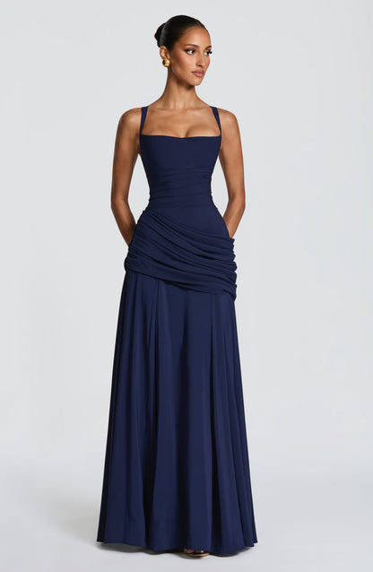 Navy dress on a model with her hands in the pockets, front view showing the draped hip panel and full skirt. 10