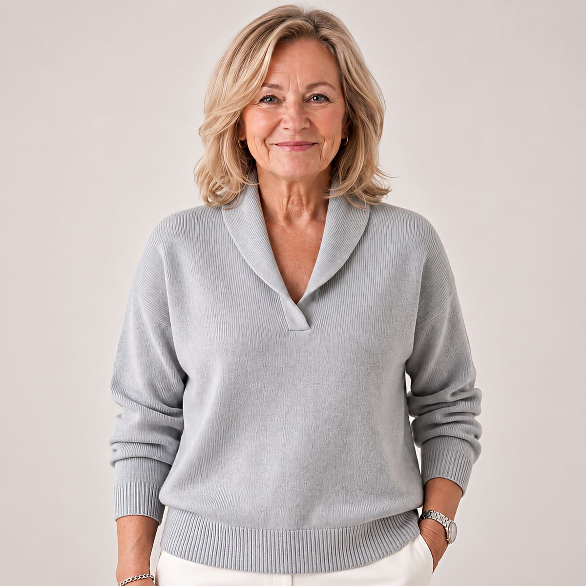 Smiling woman in the jumper in light grey, one hand in a trouser pocket, ribbed hem and cuffs visible. 3