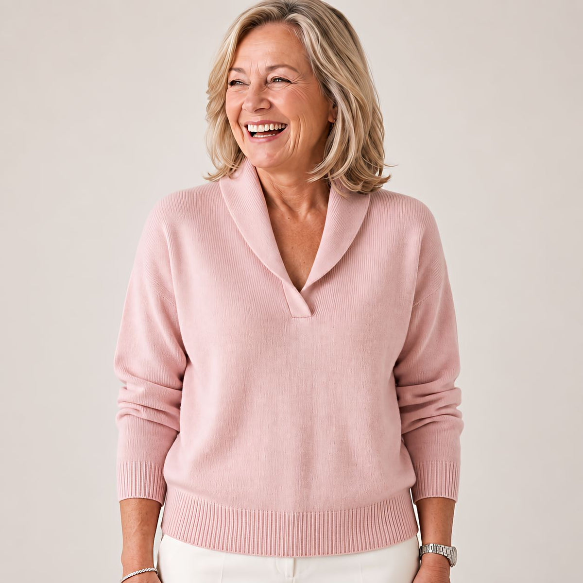 Woman laughing and looking away in the jumper in soft pink, with a ribbed hem and shawl collar. 8