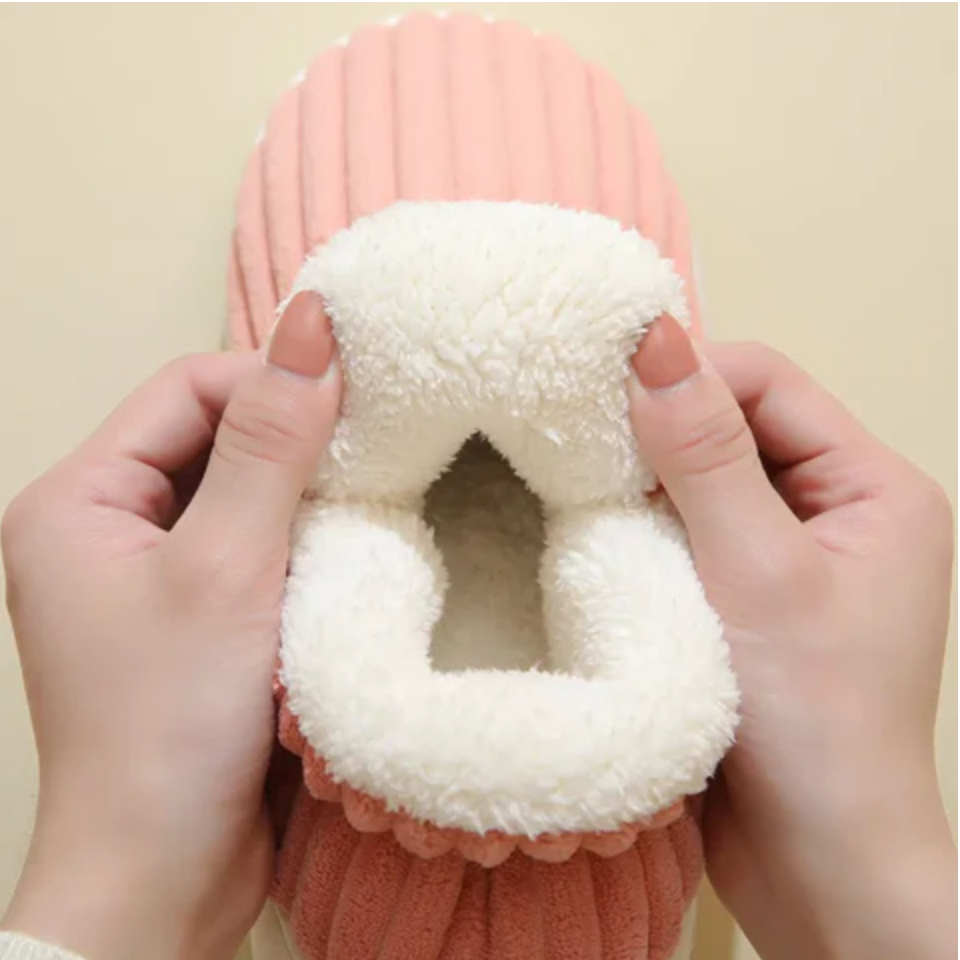 Two hands holding open a pink ribbed slipper to show the thick white fleece lining inside. 2