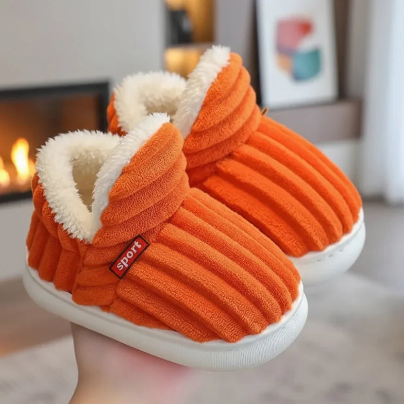 Bright orange ribbed plush slippers with white fleece lining, held in a hand near a fireplace. 8
