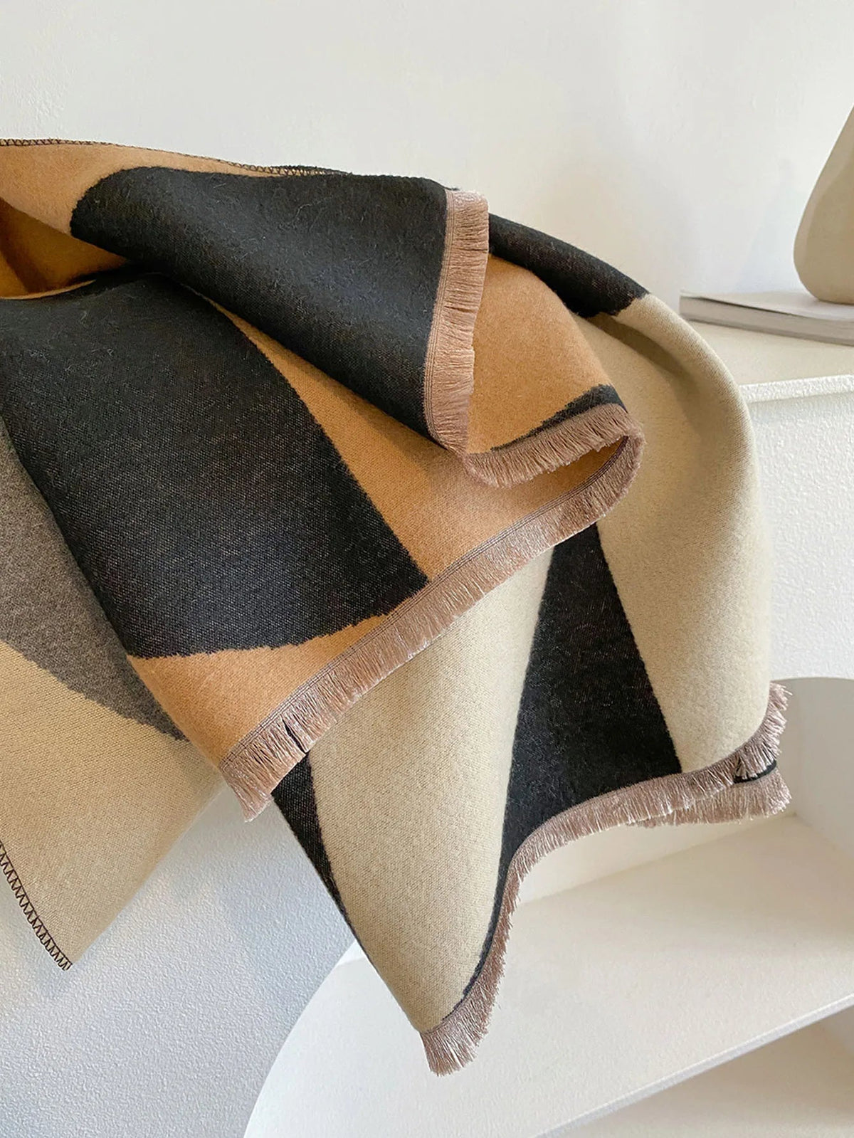 Close-up of the black, camel and cream scarf folded over, showing the soft brushed fabric and pinkish-beige fringed edge. 10