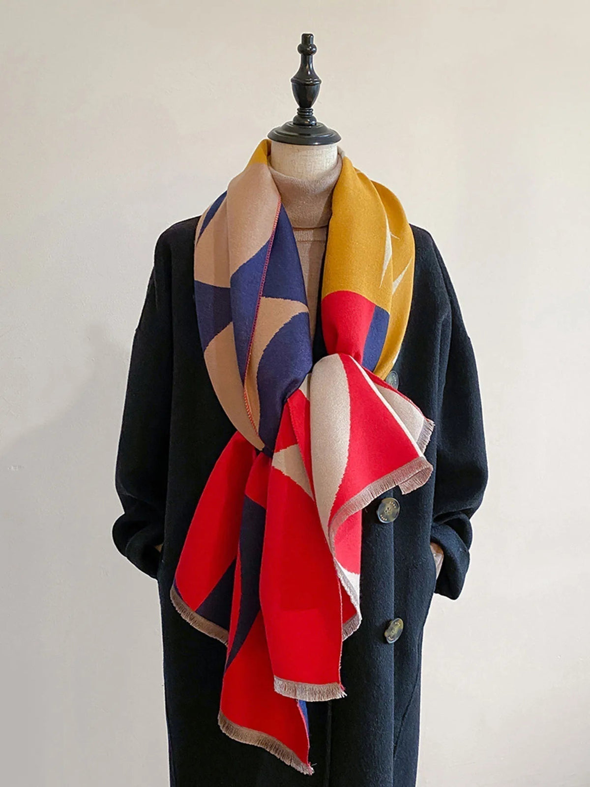 Red, yellow, navy and beige geometric scarf knotted loosely at the front of a mannequin in a black coat. 5