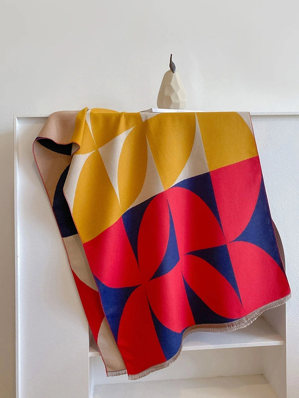 Red, yellow and navy geometric scarf hung over a white shelf unit, showing the bold quarter-circle pattern in full. 6