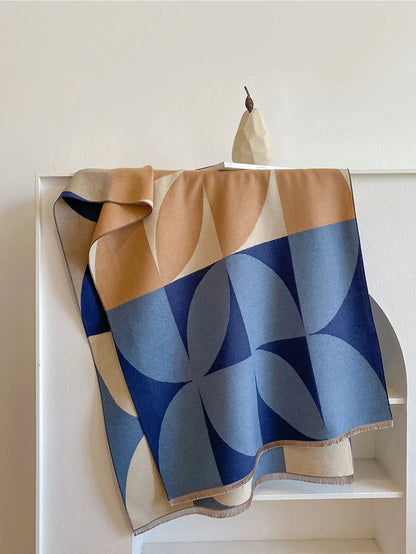 Blue and camel geometric scarf draped over a white shelf with a pear ornament, displaying its overlapping curved pattern. 7