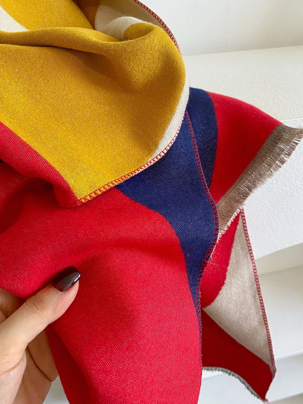 Close-up of the red, mustard and navy scarf held in a hand, showing the woven texture and contrast stitching along the edge. 9