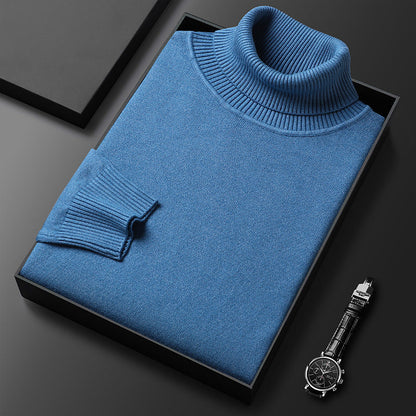 Folded blue roll-neck jumper with ribbed collar and cuff laid in a black box, with a wristwatch alongside. 2