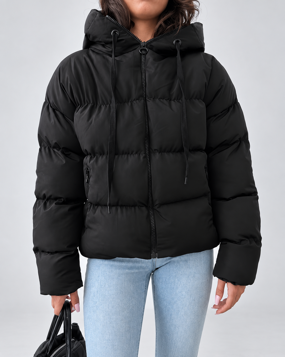 Front view of the black puffer jacket zipped up, showing hood drawstrings, horizontal quilting and zipped side pockets, worn with light jeans. 2